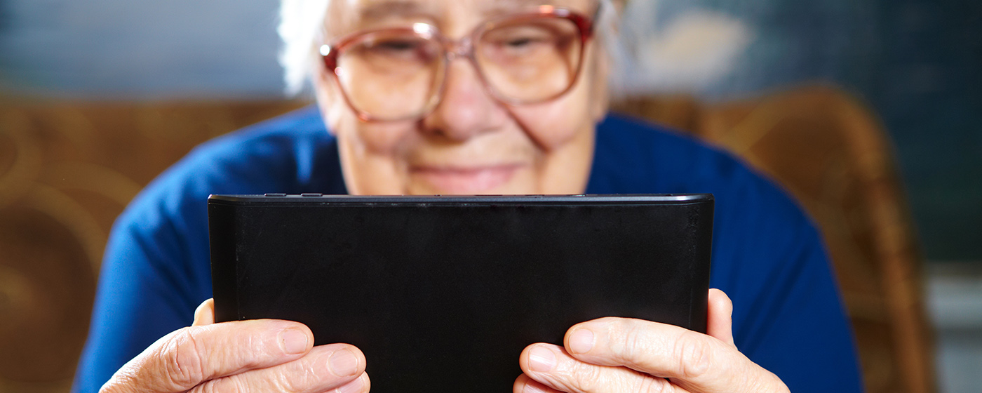 Äldre kvinna läser på en iPad 1400x560.jpg